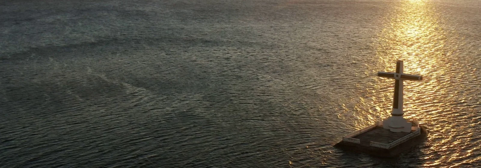Zu sehen ist ein ruhiges Meer mit Kreuz im Sonnenaufgang / Karfreitag / Ostern