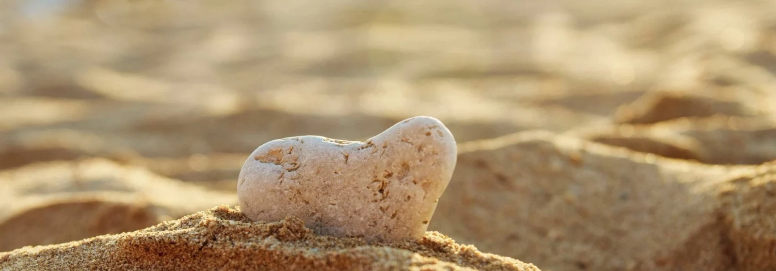 Zu sehen ist ein Stein im Sand, der wie ein Herz aussieht / Küstlich