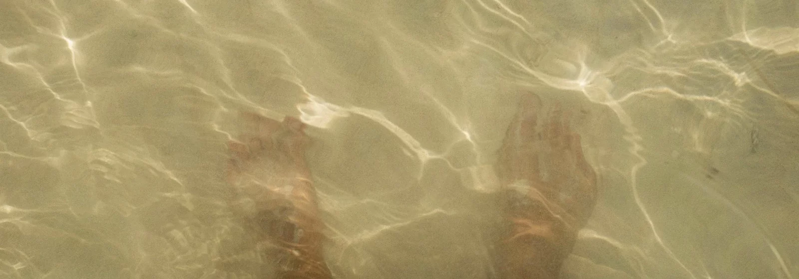 Zu sehen sind Füße im flachen Meerwasser als Sinnbild für einen mutigen nächsten Schritt / Trotz-Gut